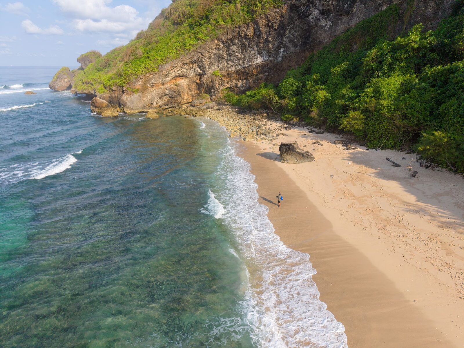 A sheltered cove of soft sand backed by green cliff.