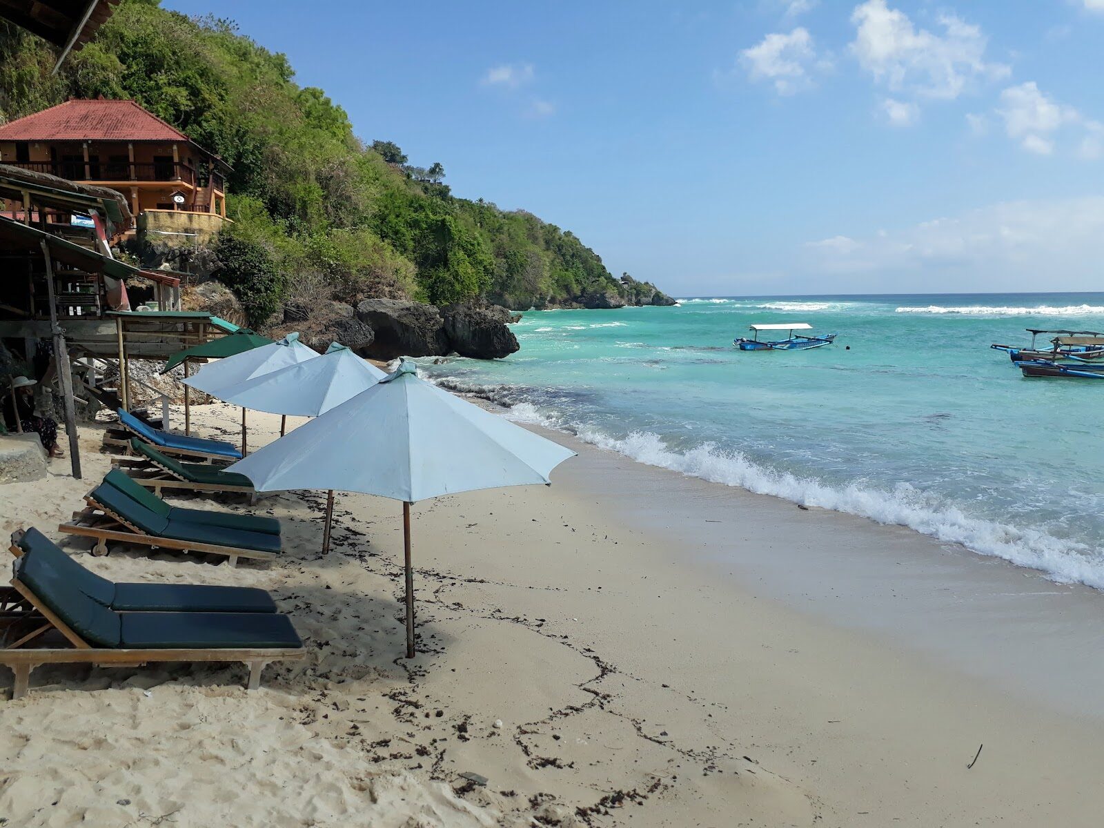 Thomas Beach — loungers and an umbrella on calm turquoise water, boats moored offshore.
