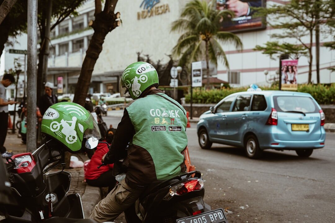 A Gojek rider crouches by his bike beside a waiting car — the two big apps do both bikes and cars.