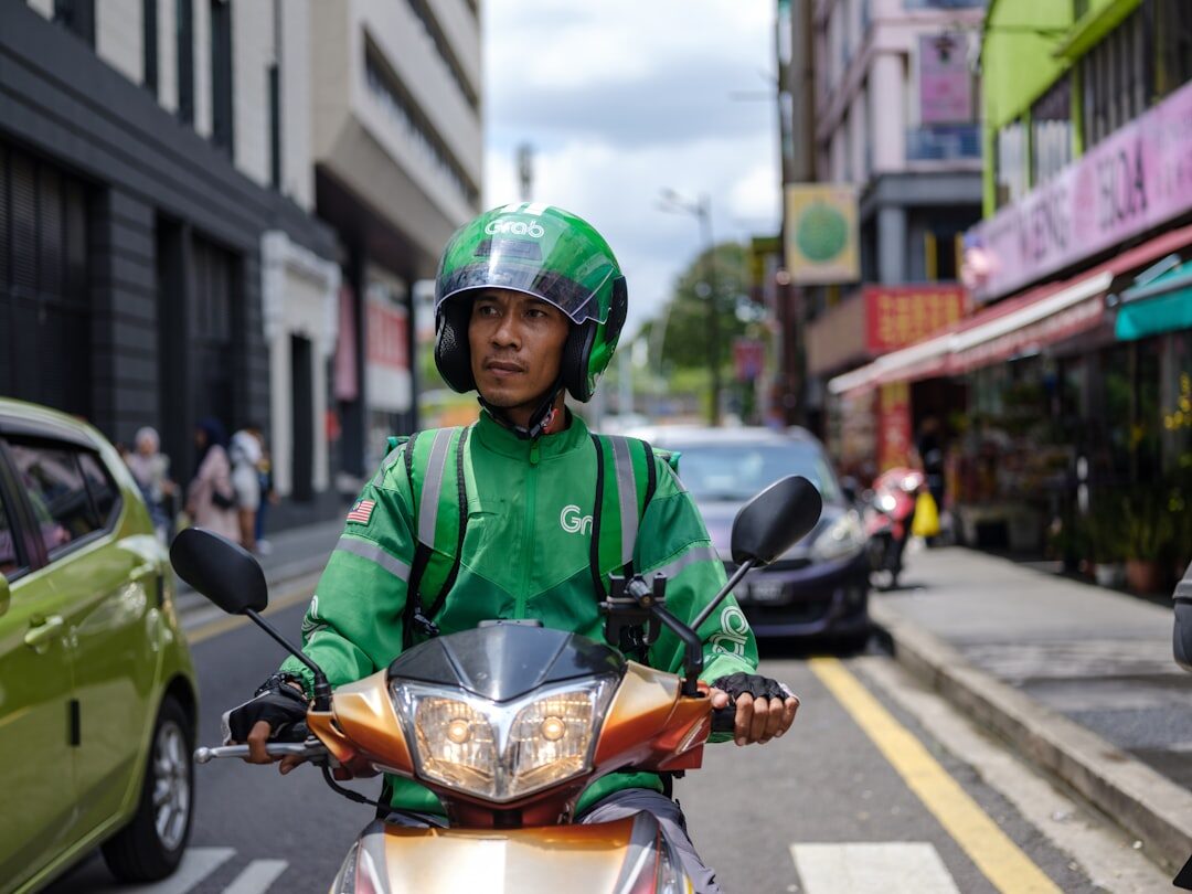A green-jacketed ride-hailing rider works his way down a city street.
