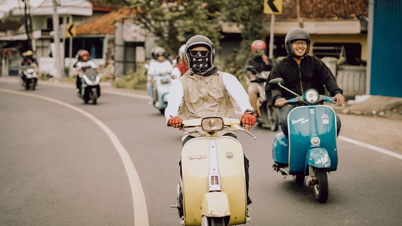 A group rides Vespas in helmets on a country road.