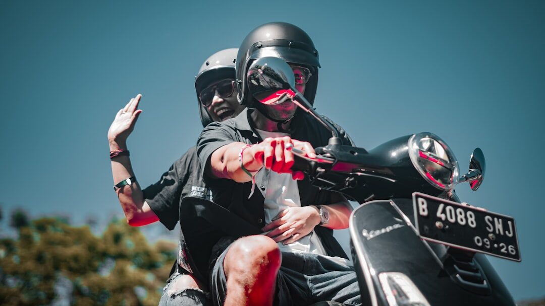 Two riders in full-face helmets on a scooter — the gear that's legally required for rider and passenger both.
