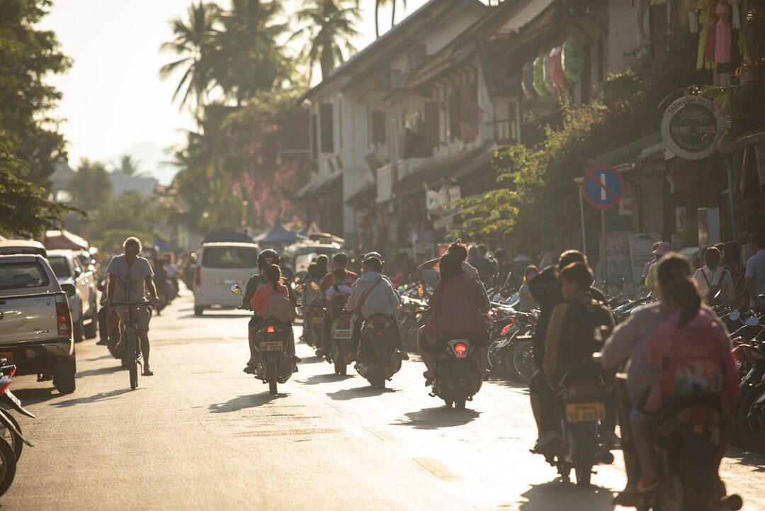 Parked scooters and riders along a shophouse street.