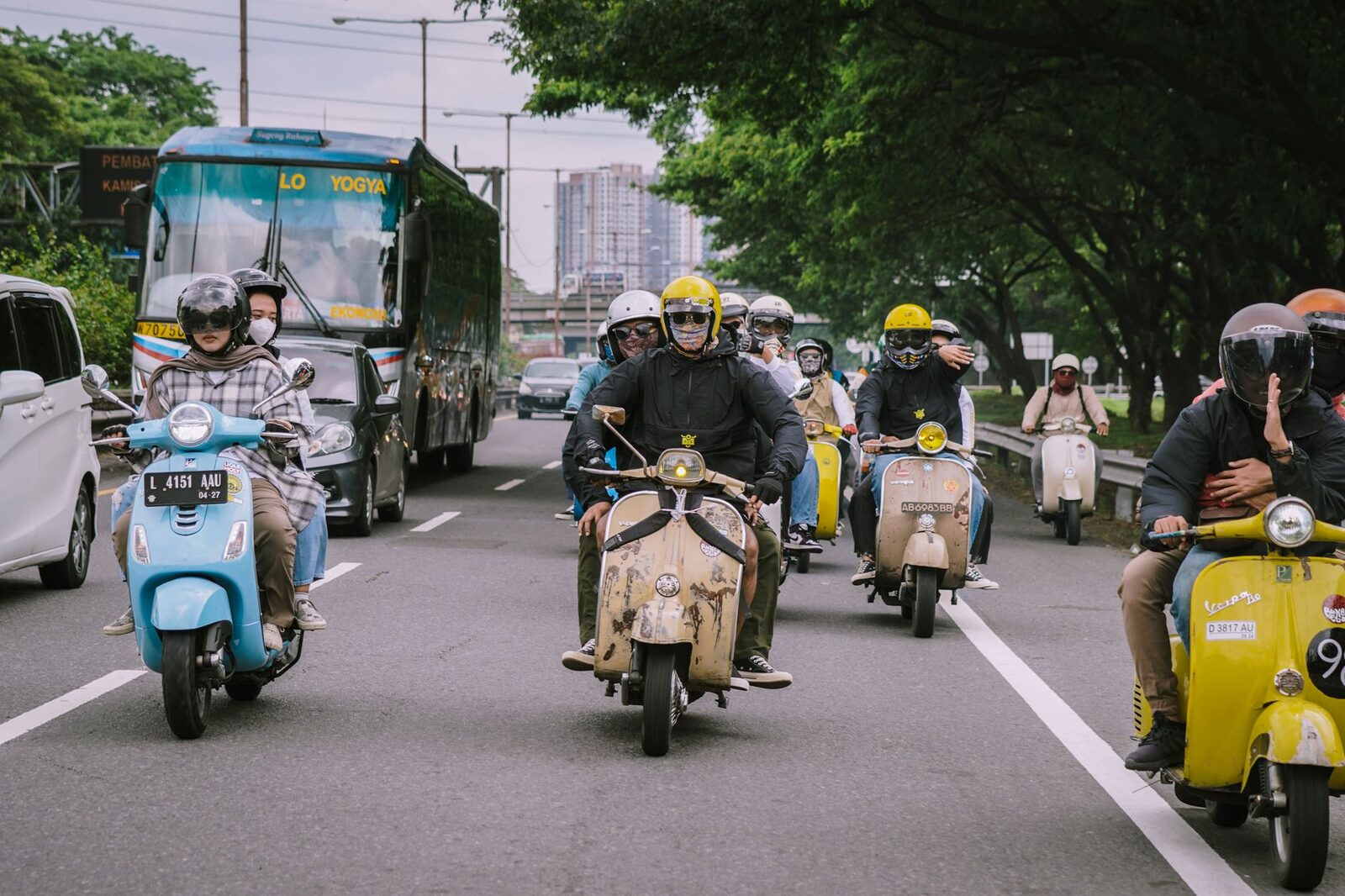 A knot of riders comes on down the road, scooters and a laden truck among them.