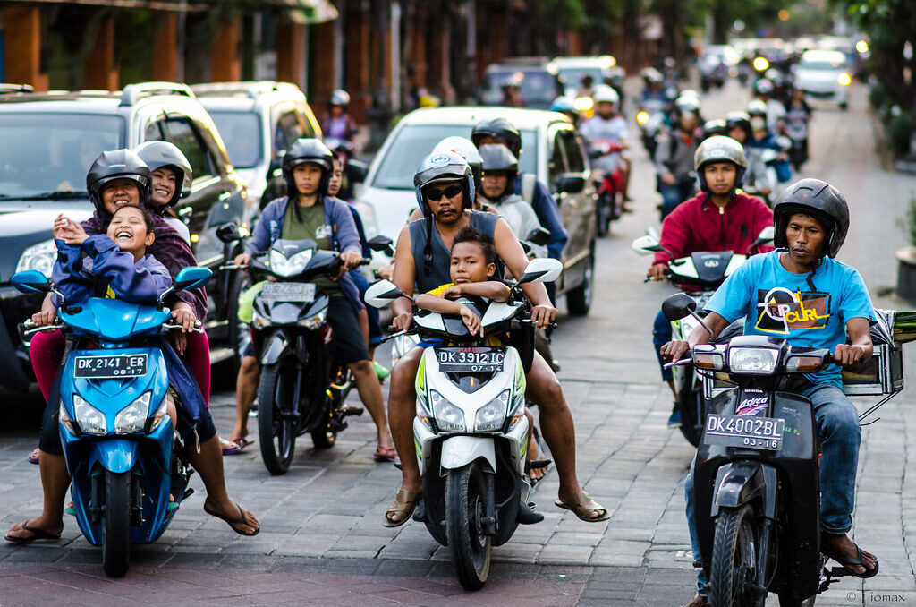 Oncoming scooters pack a Bali street, whole families aboard — the unorderly flow you actually ride in.