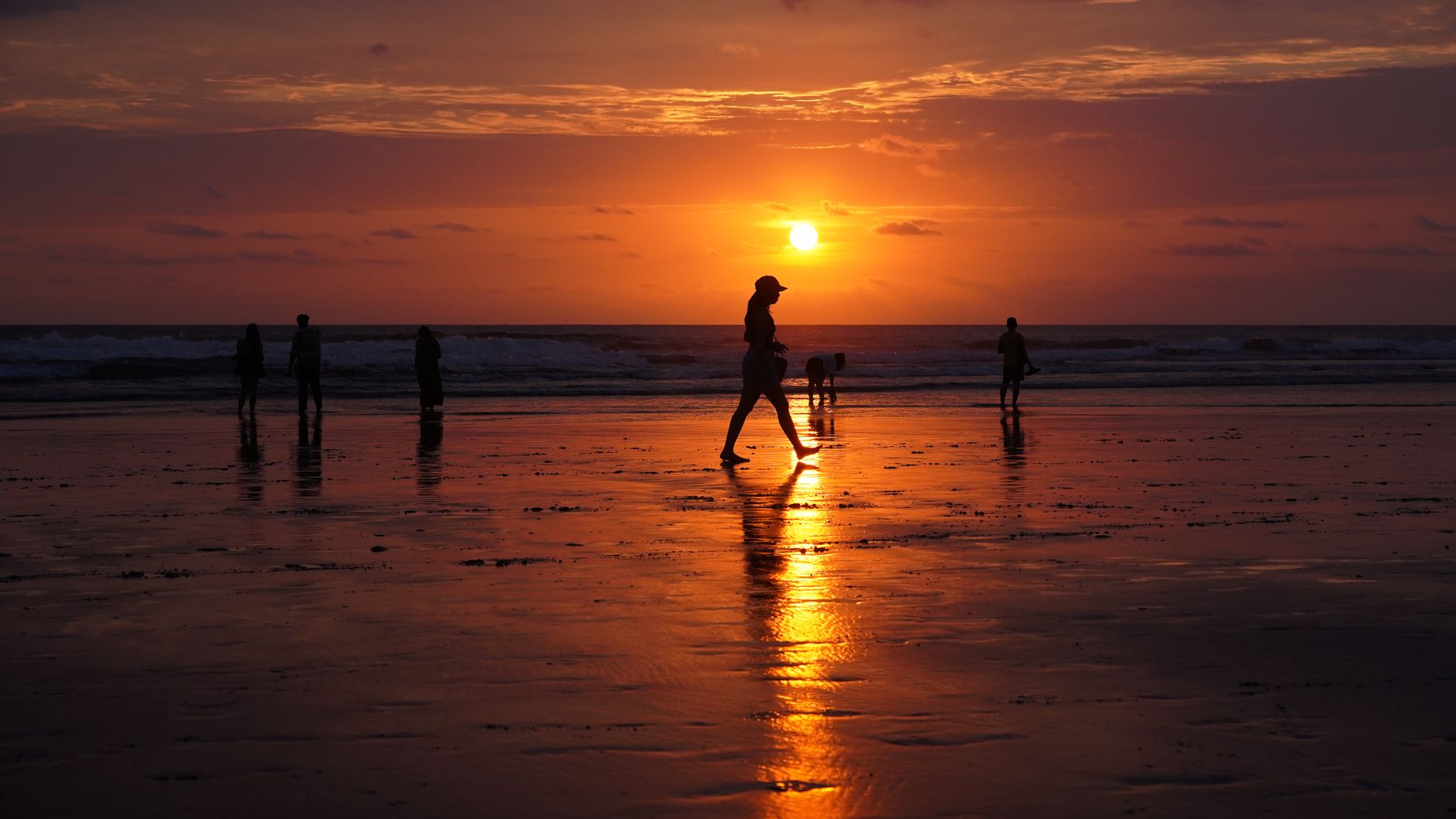 People walking a serene Seminyak beach at sunset