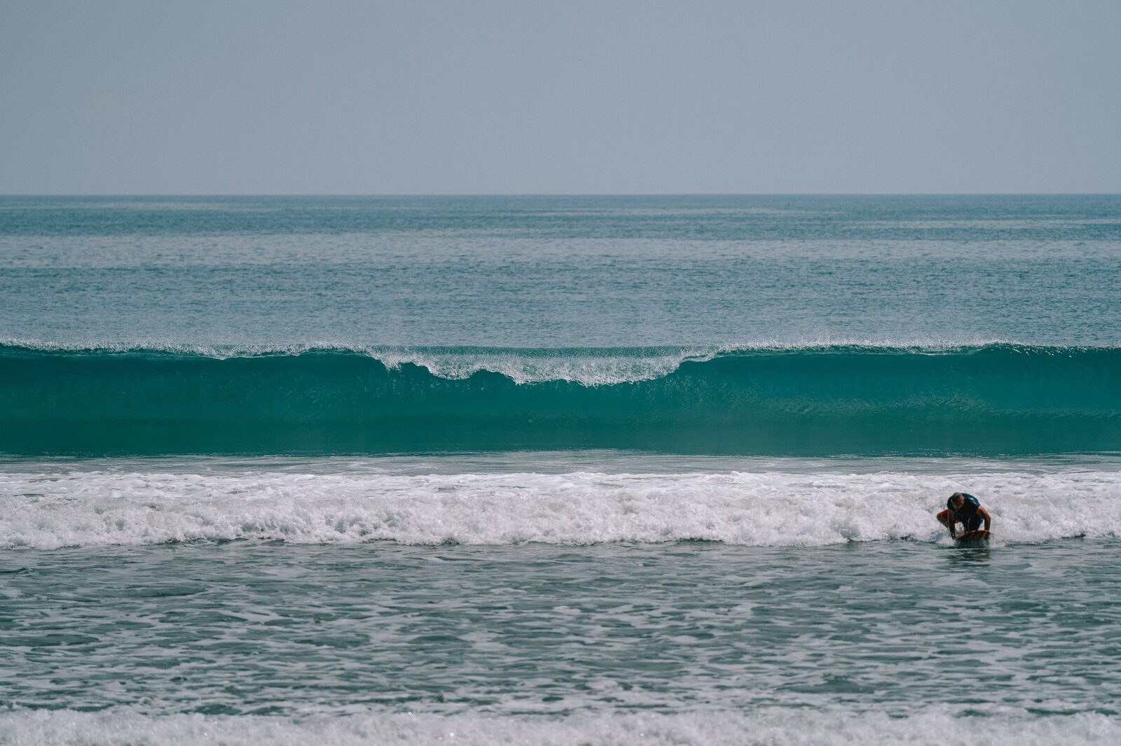 A single rider on a soft, rolling wave at a sandy beach break.