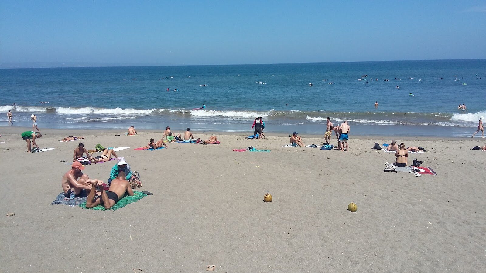 A busy sand beach on the west coast, surf schools and swimmers sharing the water.
