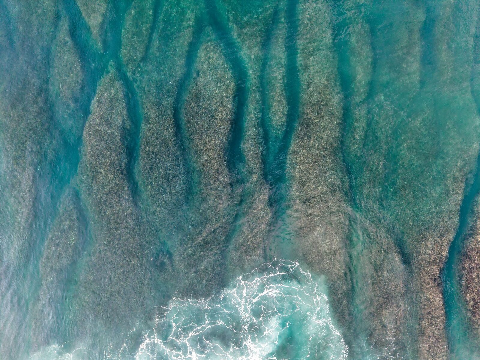 Aerial texture of a shallow reef, channels of sand and coral just under the surface.