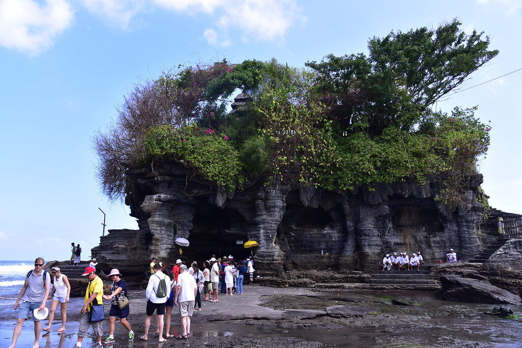 A line of visitors on the rocks below the temple — shoulder to shoulder in season.