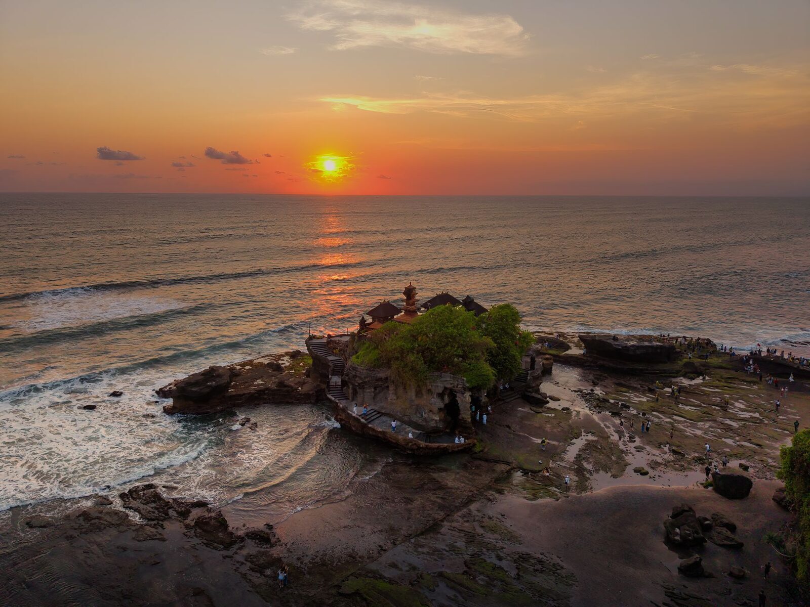 The sun on the horizon, orange light across the sea beyond the rock.