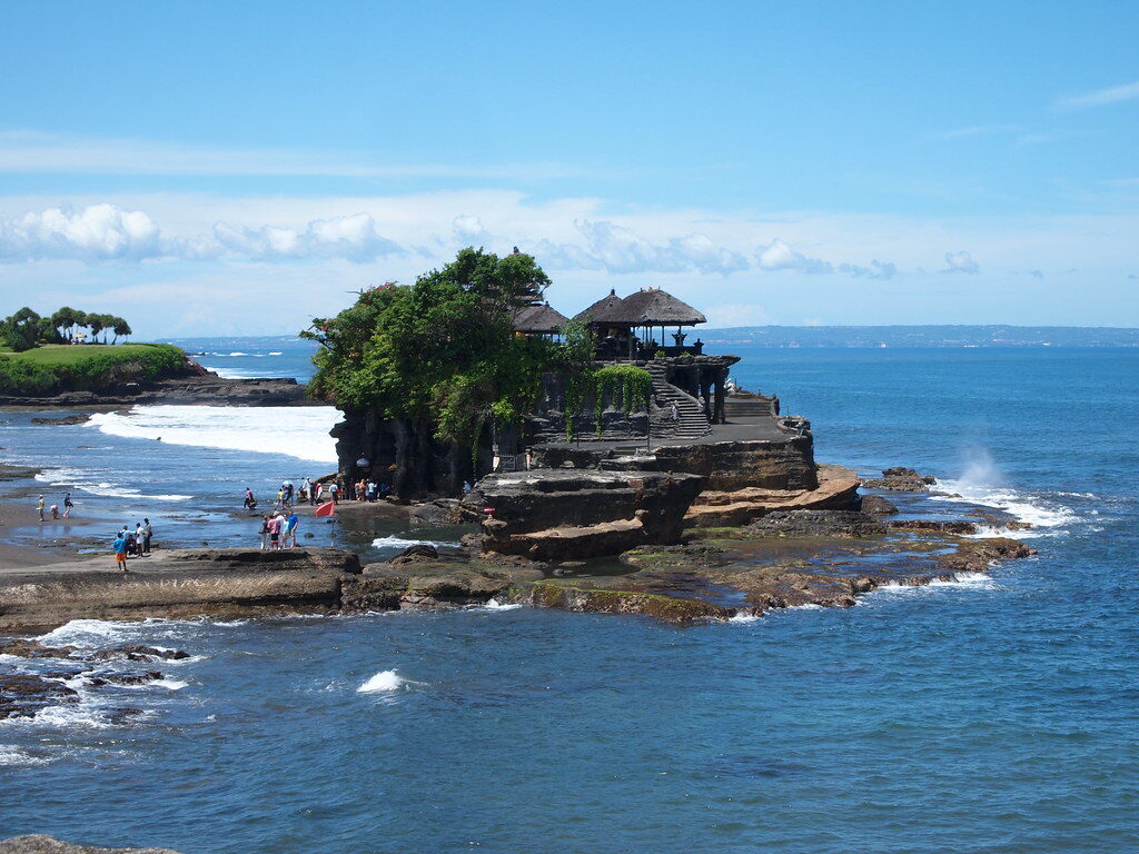 The temple islet ringed by blue water, seen across the rocks at its foot.