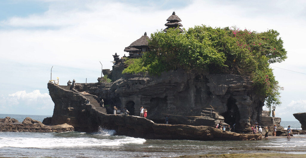 The temple perched on its weathered outcrop, palms and shrines on top.