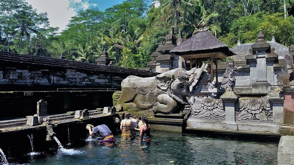 Temple grounds beside one of the pools, a carved guardian standing over the water.