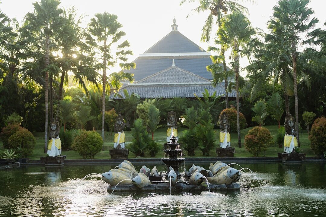 The fountain with a garden pavilion and palms behind it in soft light.