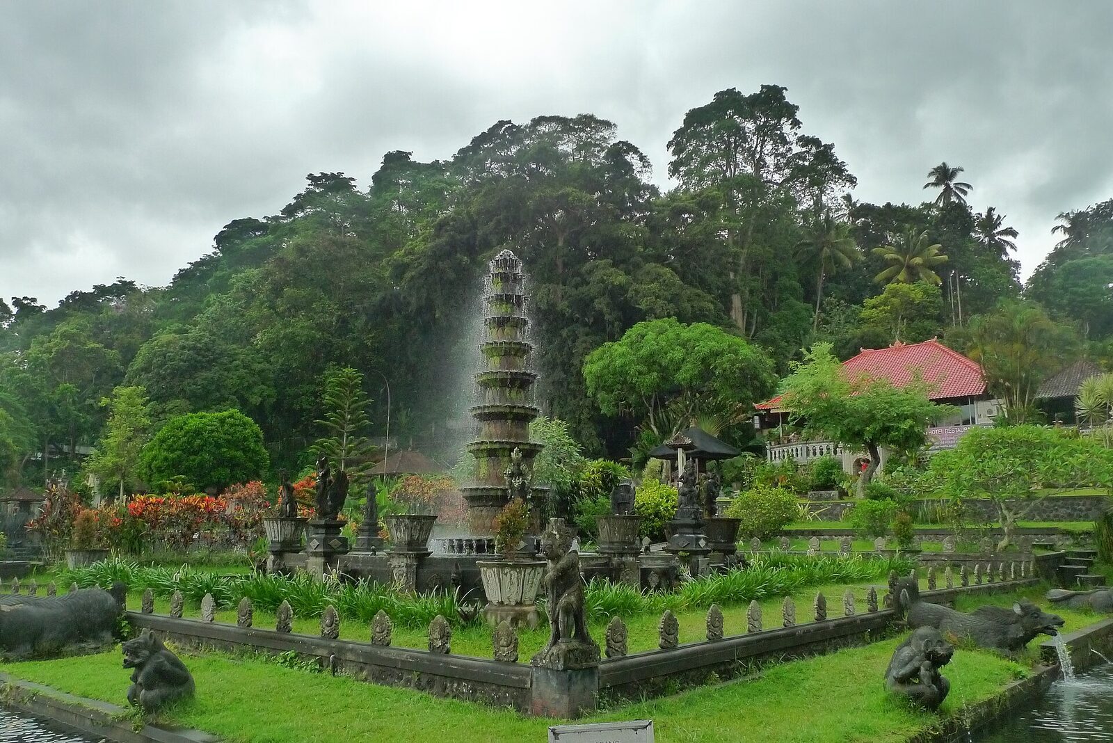 The fountain in full spray after rain, the garden lush behind it.