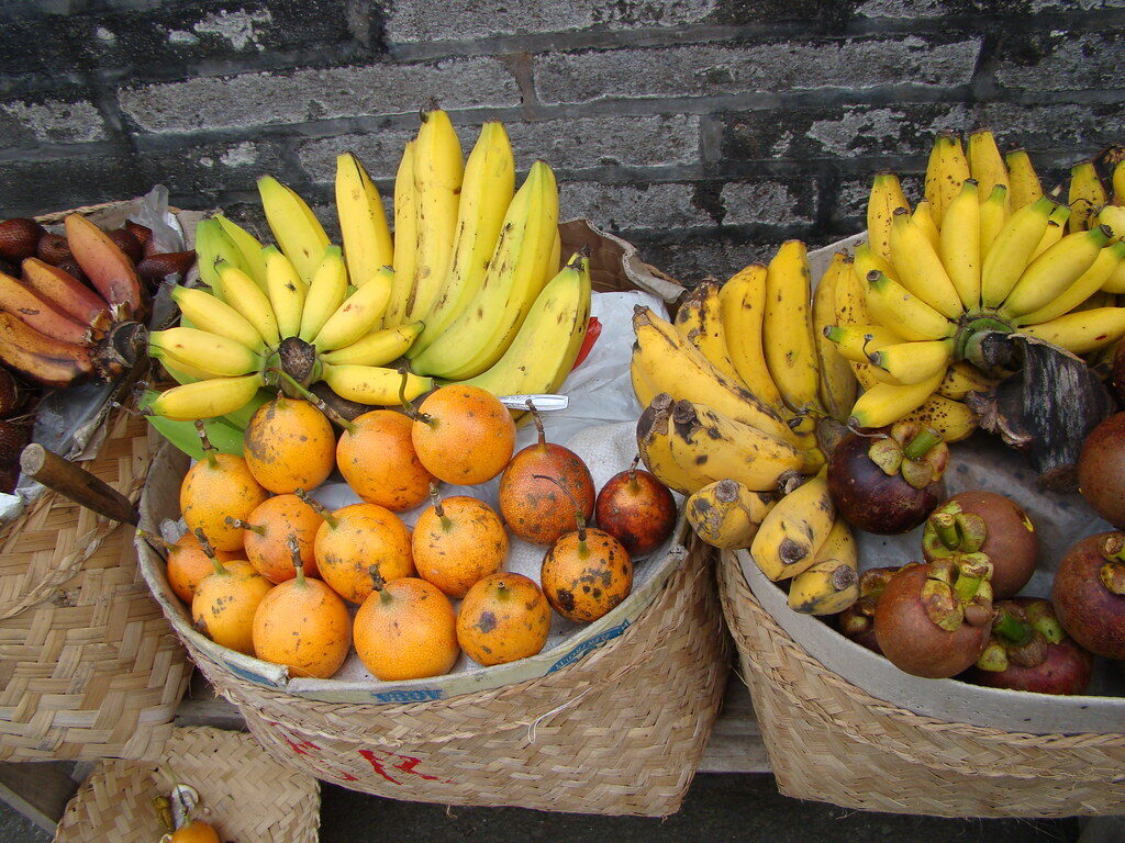 Fruit baskets at a market stall — bananas and oranges by the pile.