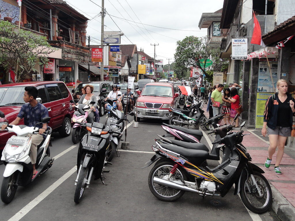 Scooters lining the kerb and a car nosing through — the congestion that starts by mid-morning.