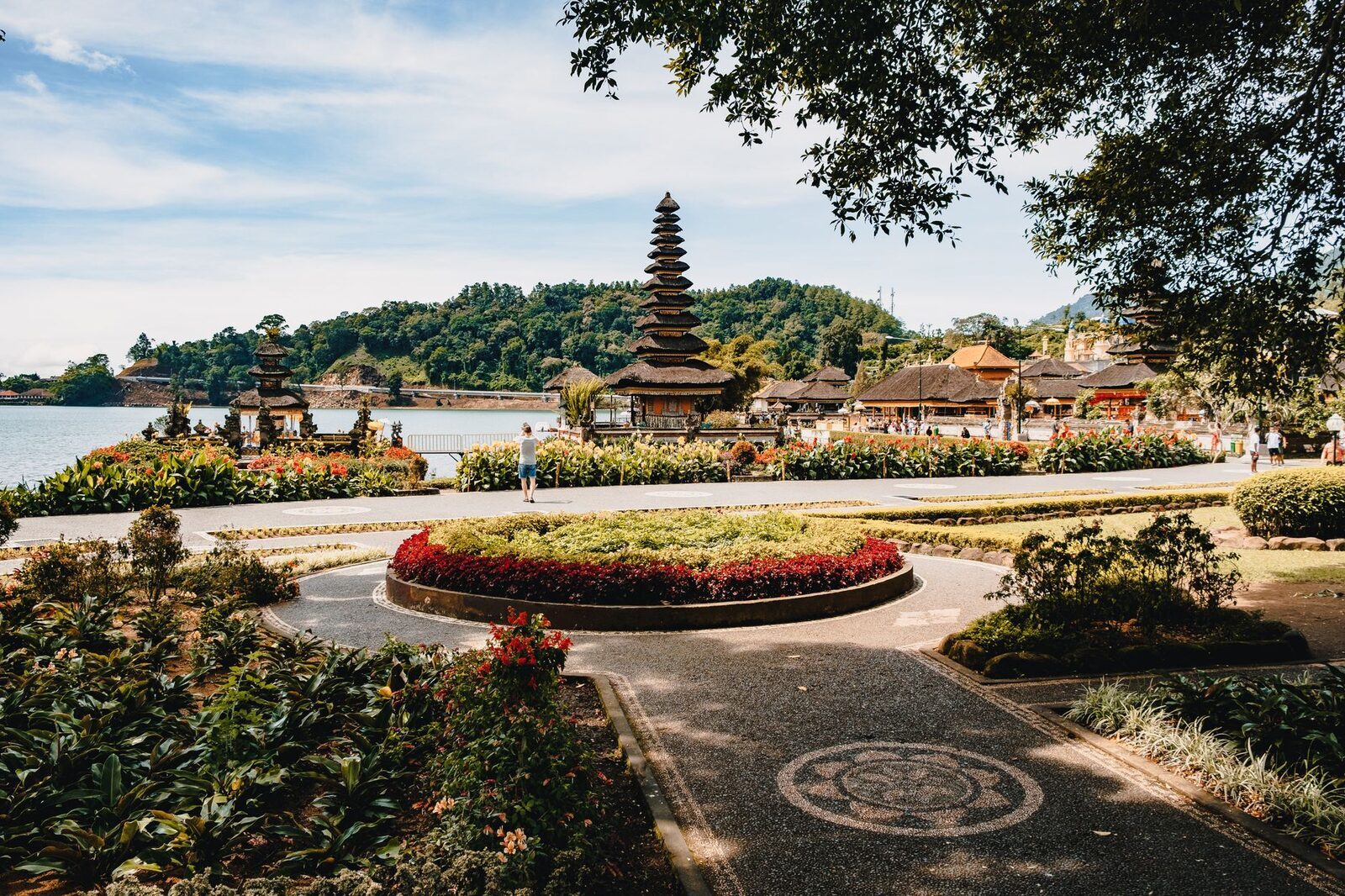 Paved paths and a round flower bed in the landscaped grounds, the meru small beyond.
