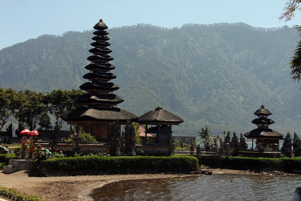 The shrine and its thatched pavilions on the water, the forested highland ridge rising behind.