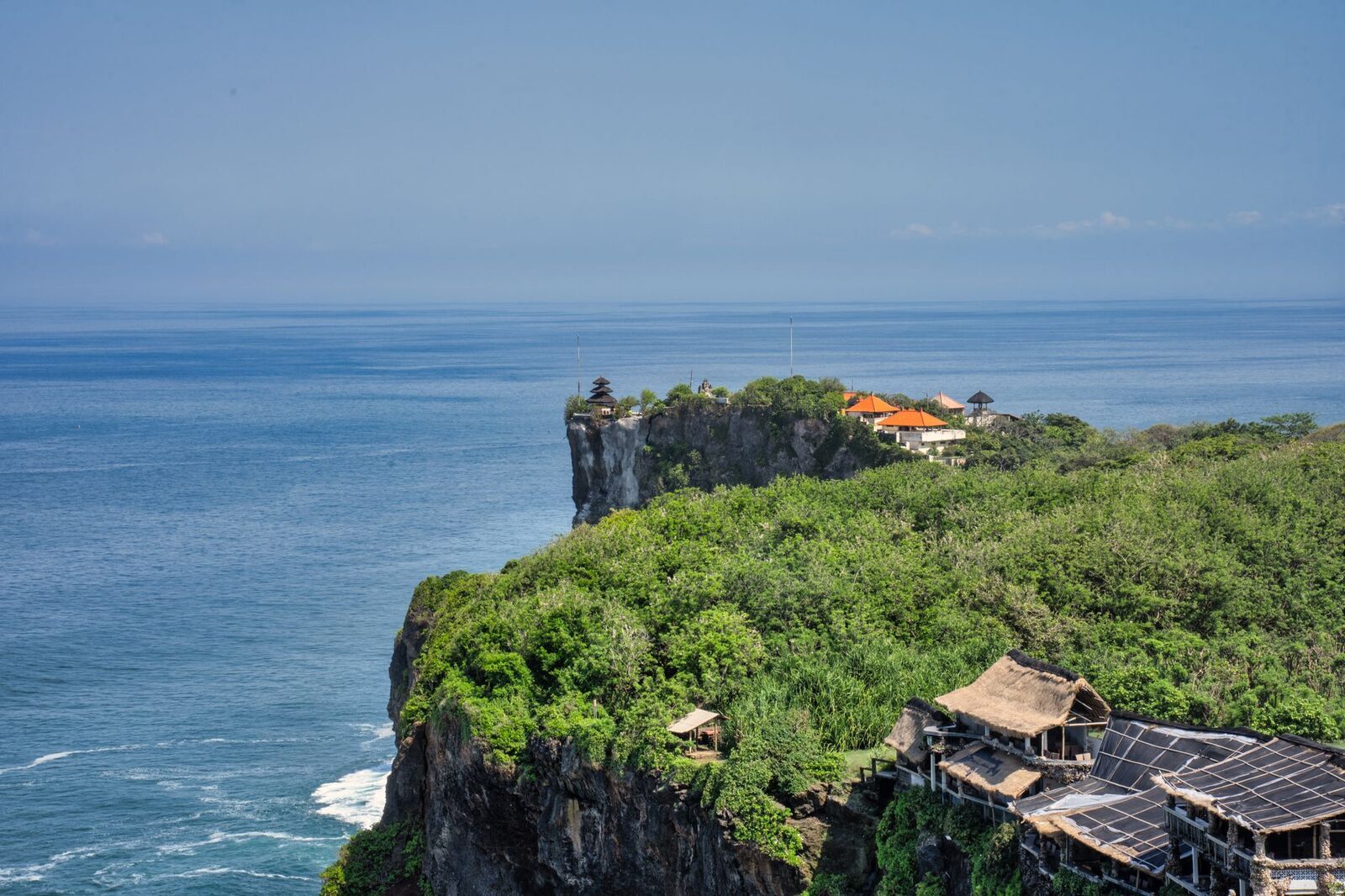 The temple's structures perched on the cliff, small against the drop.
