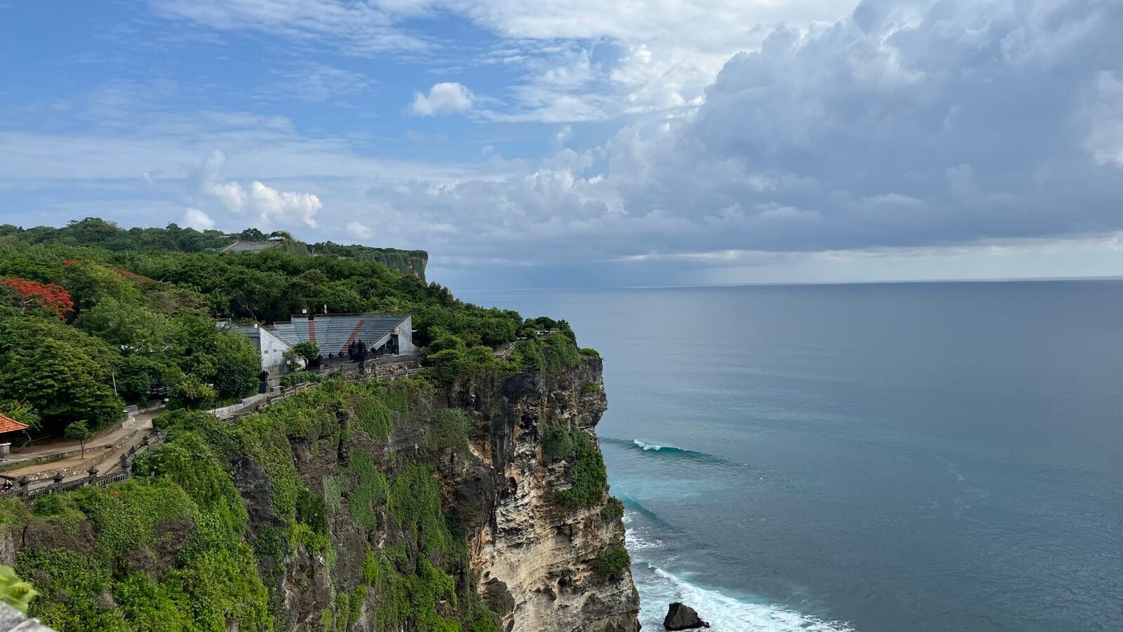 Pavilions perched on the cliff, a calm sea beyond.