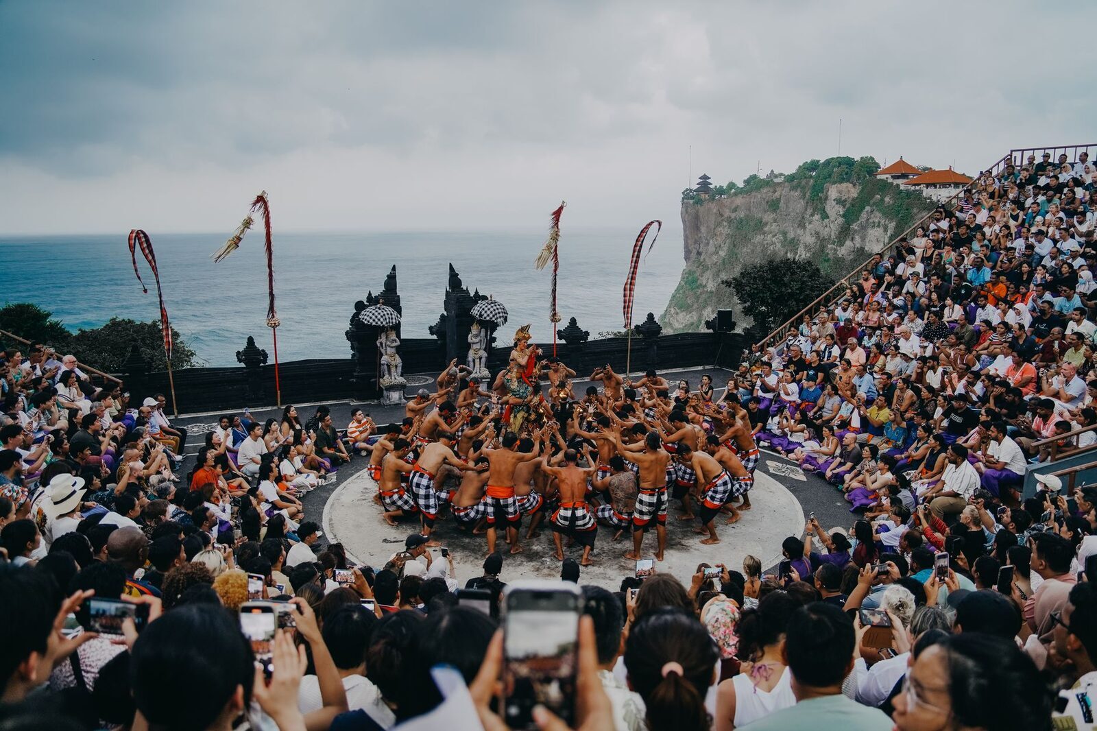 A full house at dusk, the crowd wrapped around the ring with the sea behind.