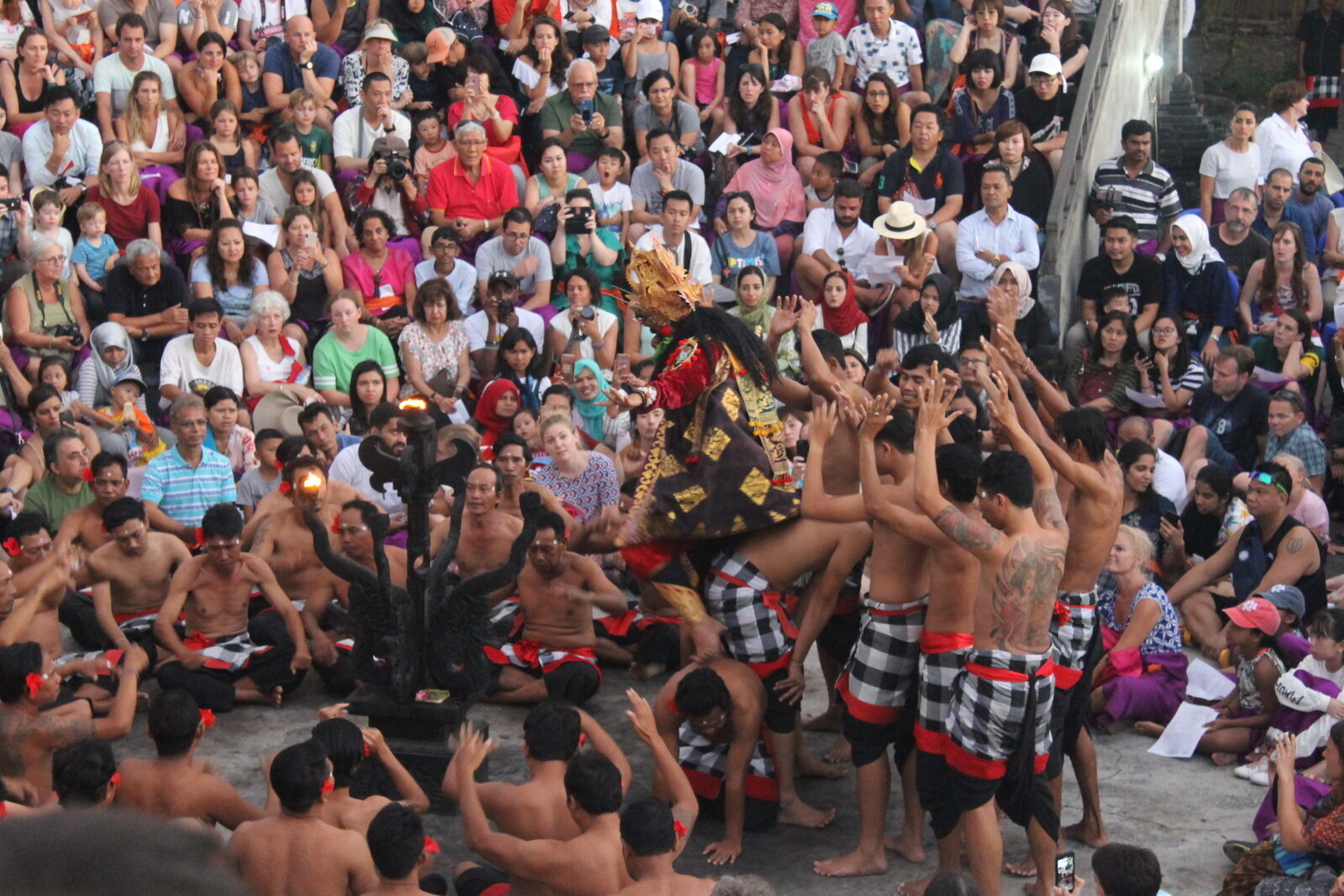 The Uluwatu Kecak in daylight: the chorus ringed around the dancers, the crowd banked behind.