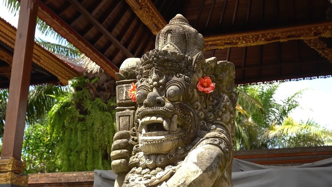 A grotesque stone guardian sheltered under a pavilion, a hibiscus tucked behind its ear.