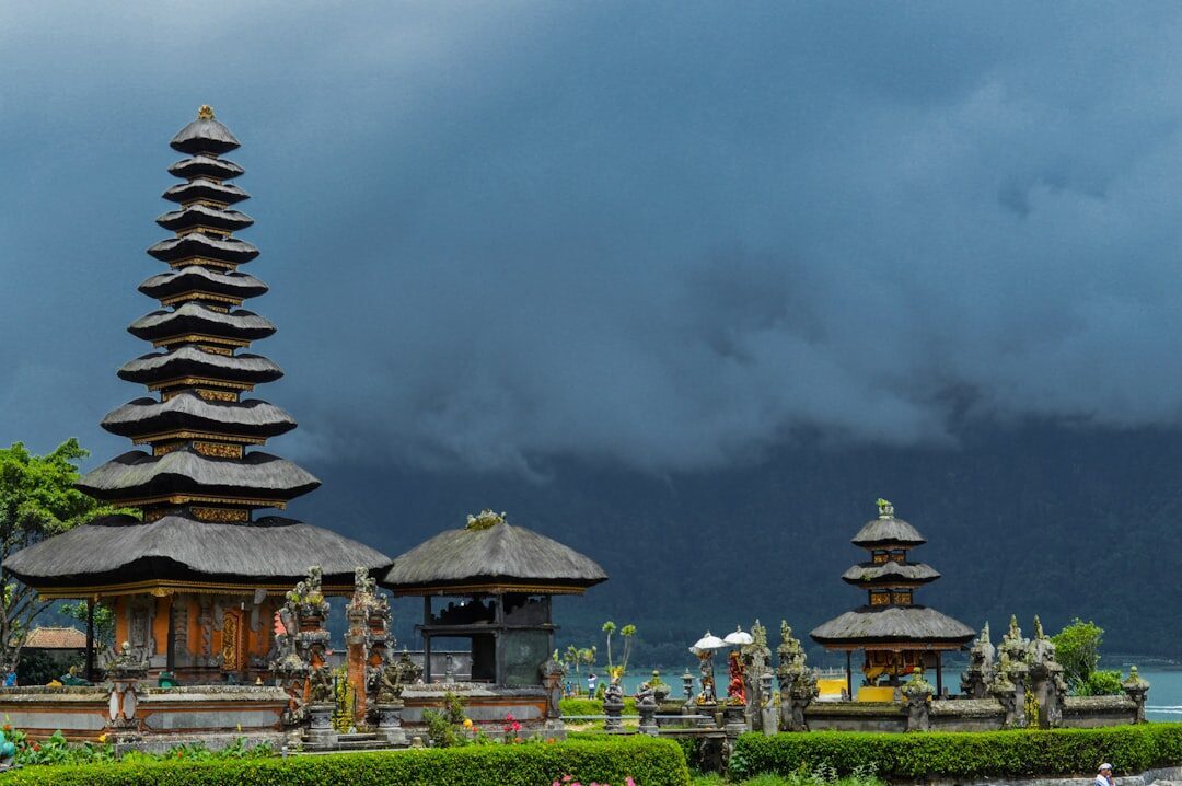 Meru towers under a gathering storm, palm-fibre roofs stacked in odd tiers.