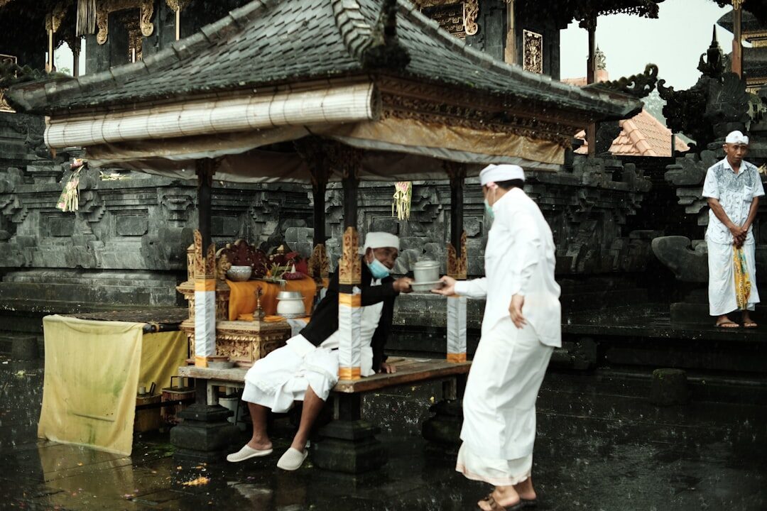 Priests in ceremonial white tending an altar of offerings at a Balinese shrine.