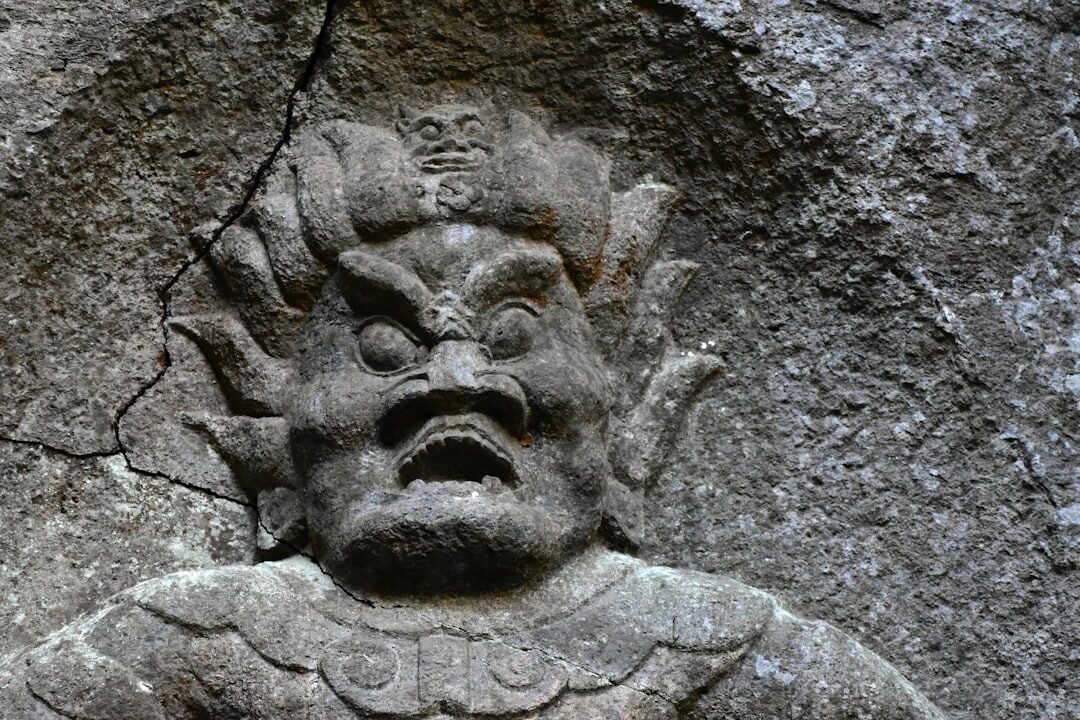 A weathered grey carved face, its edges still crisp in hard stone despite the cracks of age — the kind of durability Uluwatu's coral limestone gives its carvings.