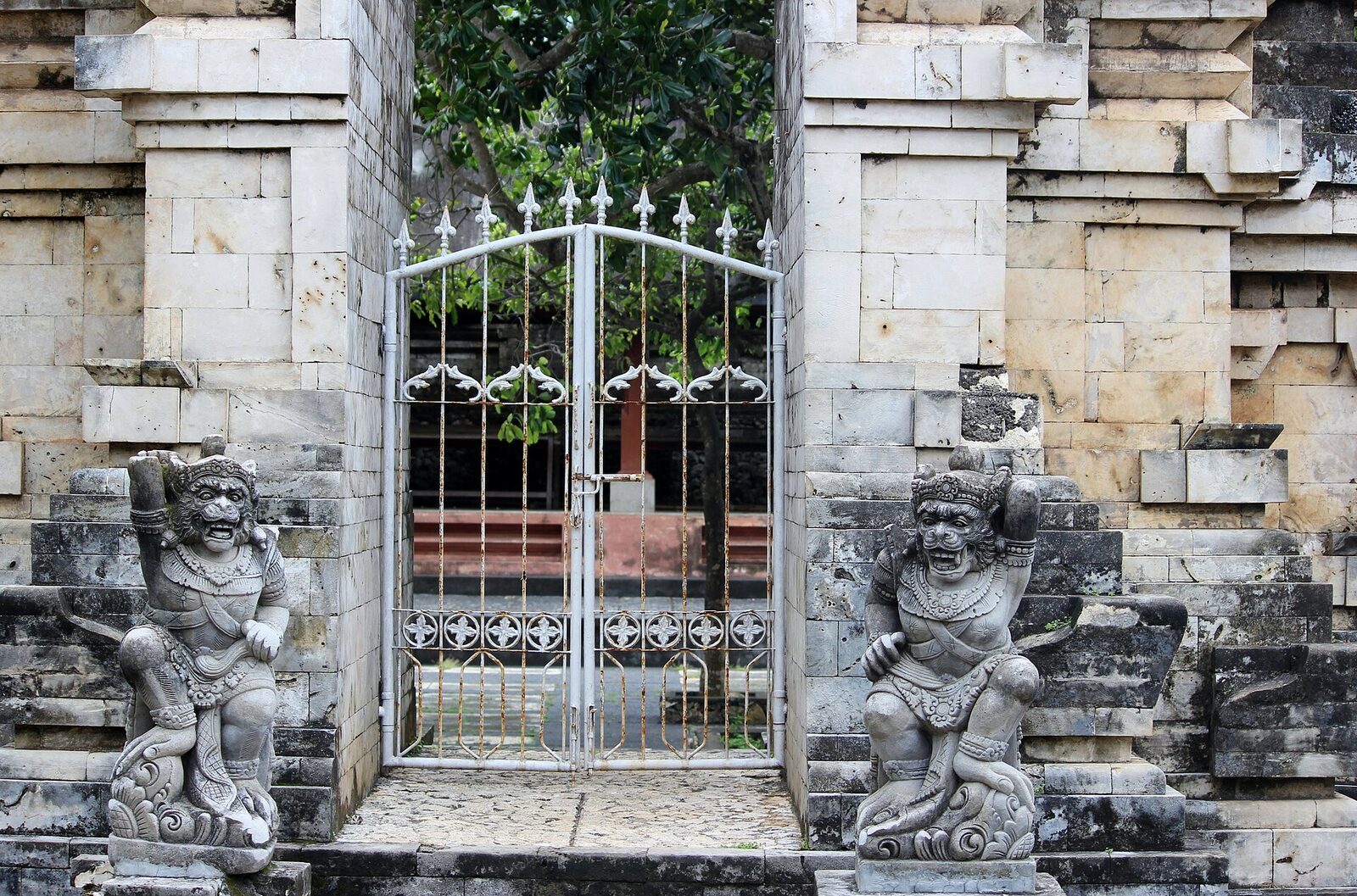 A split gateway flanked by two stone guardian statues at Uluwatu temple