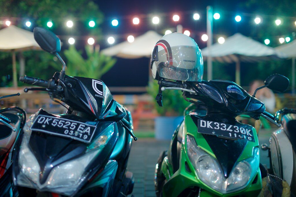 Scooters parked three-deep outside a lit-up beach club after dark — Canggu's nightlife and its traffic in one frame.