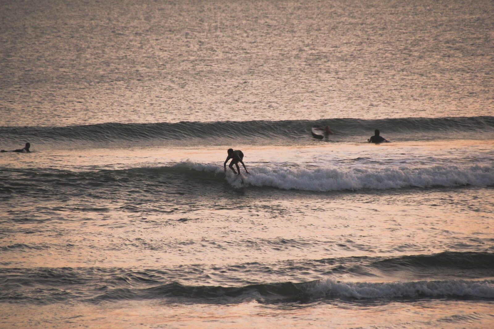 Surfers still out at sunset — the water stays busy right to dark.