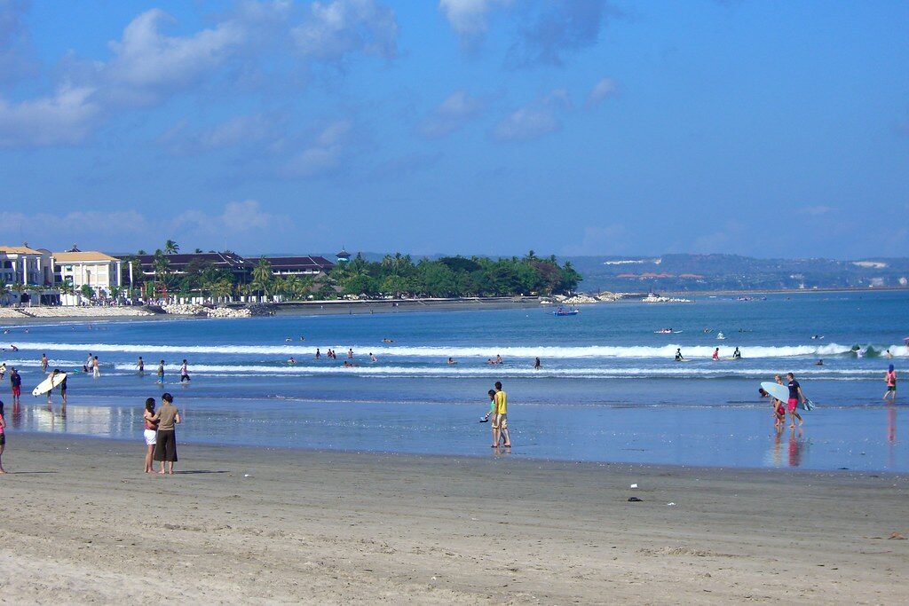 Kuta's long, wide beach — the island's big learn-to-surf break, with the hotel strip stacked up behind it.