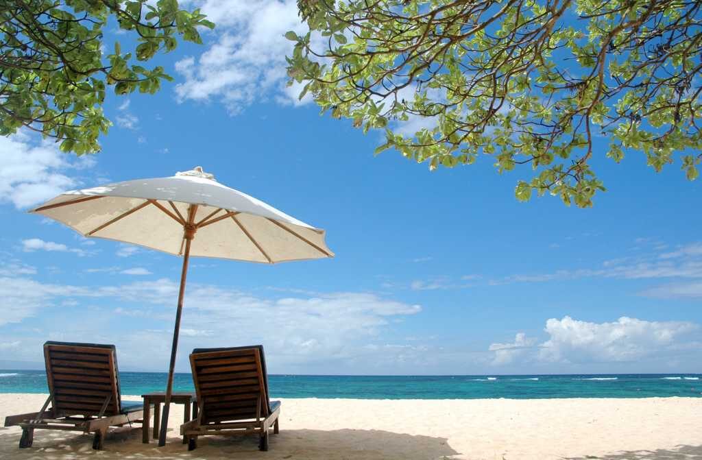 Loungers under an umbrella on a calm, clear bay — the gentle, everything-handled version of a Bali beach that Nusa Dua and Jimbaran do best.