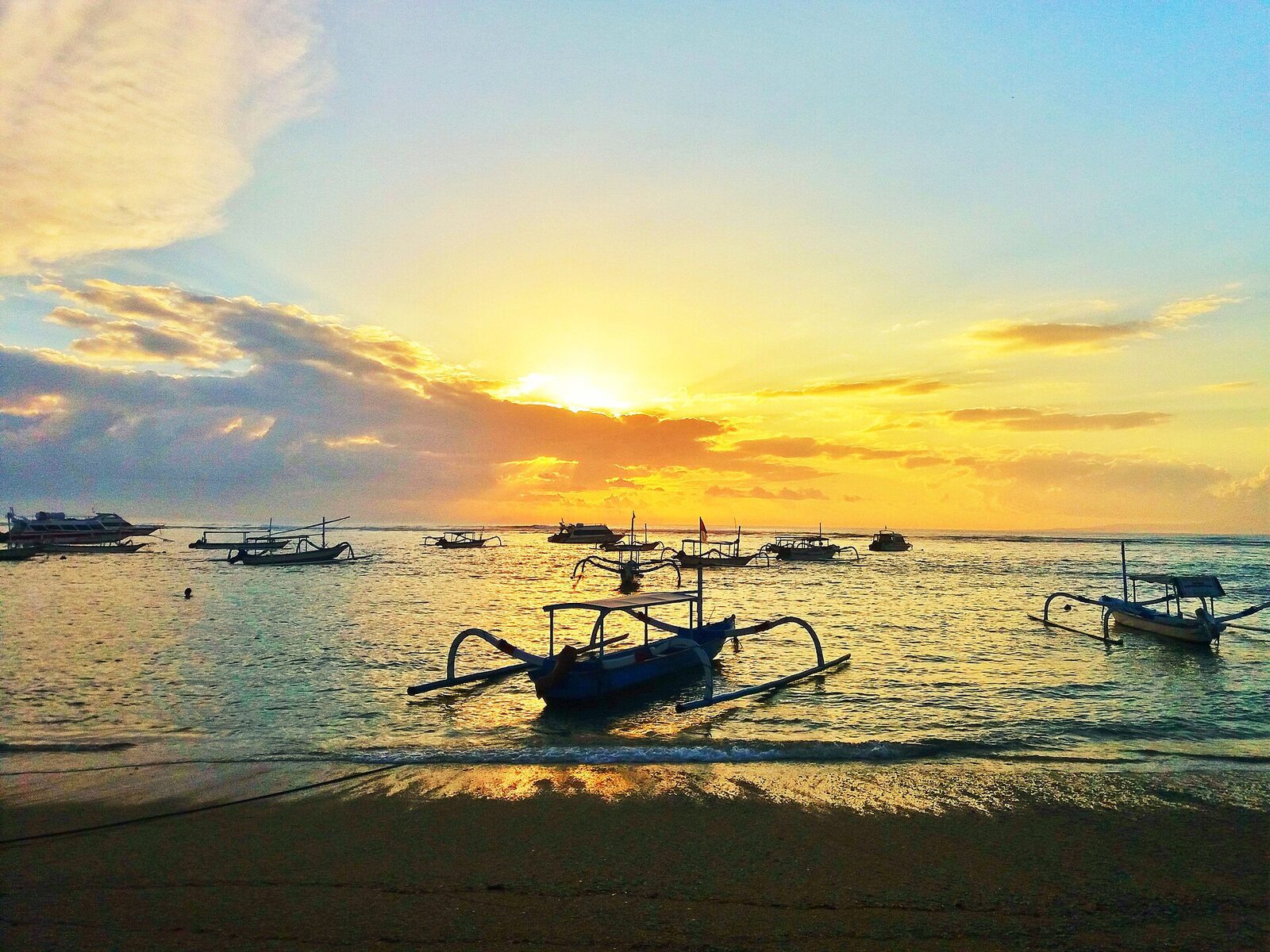 A jukung outrigger on the sand as the sun comes up over Sanur — this is a sunrise coast, calm and slow where Canggu is loud.