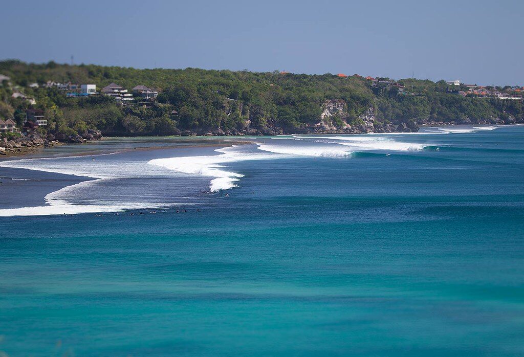A turquoise reef bay with houses stacked on the headland above — the Bingin-and-Padang stretch the surf world flies in for.