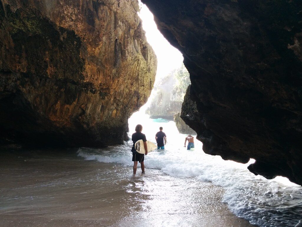Visitors wading out through a sea cave to a hidden cove — the kind of access the Bukit is known for.