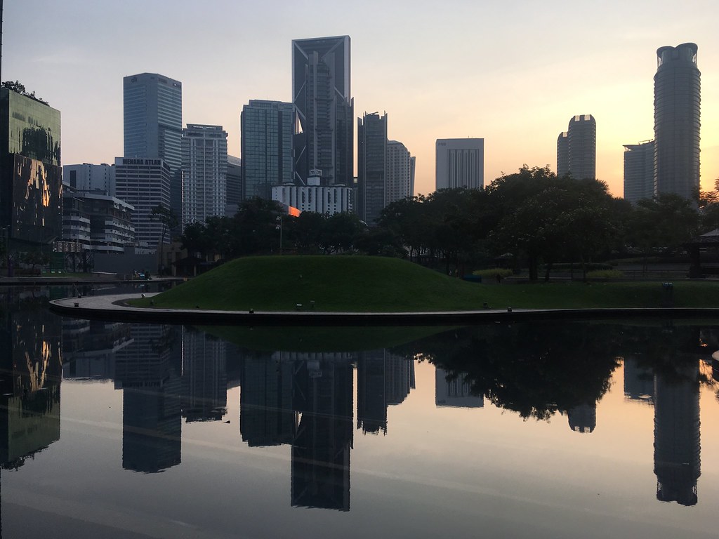 The Petronas Towers above the lake and greenery of KLCC Park at golden hour.